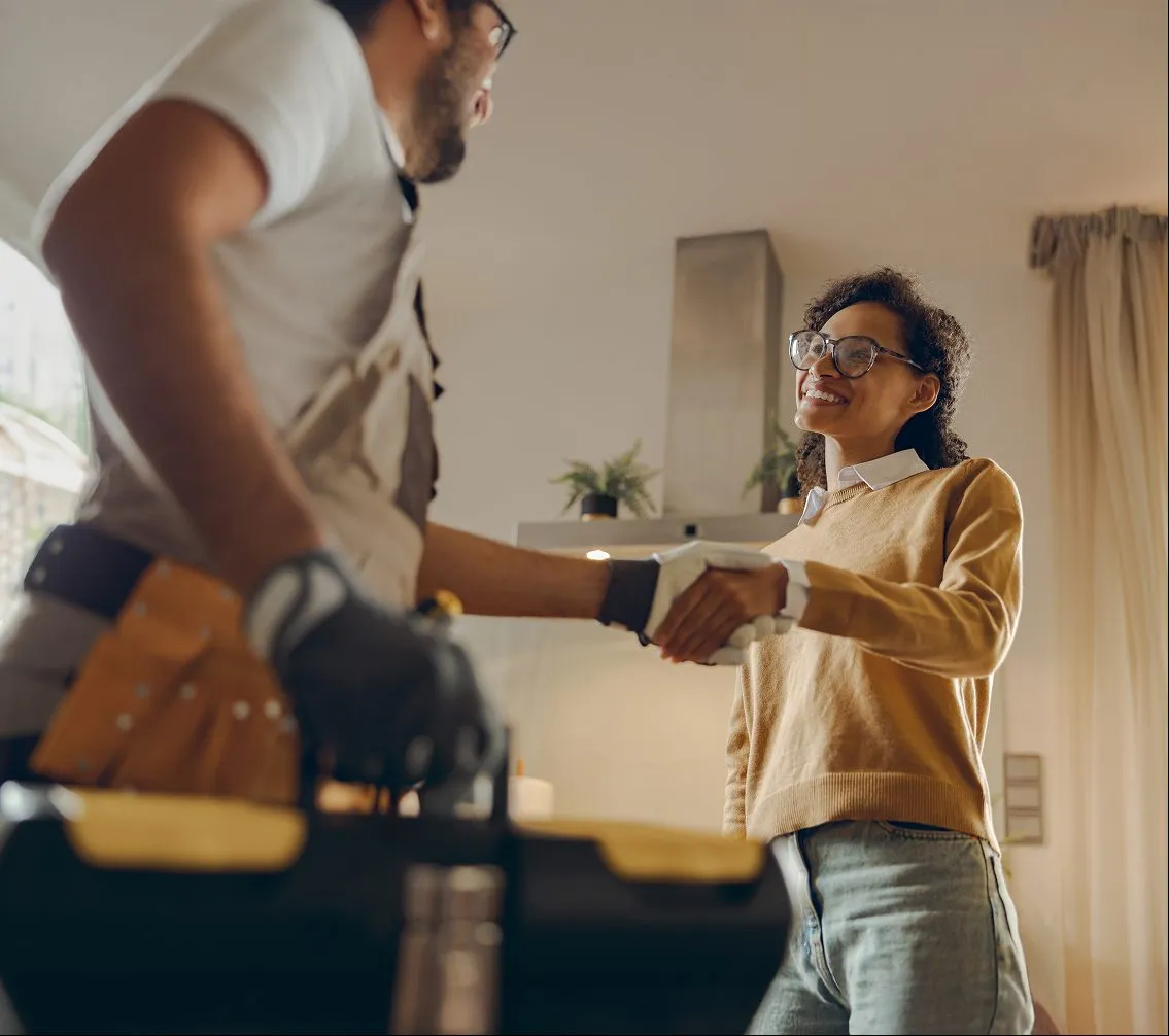 A contractor in a tool belt shaking hands with a homeowner