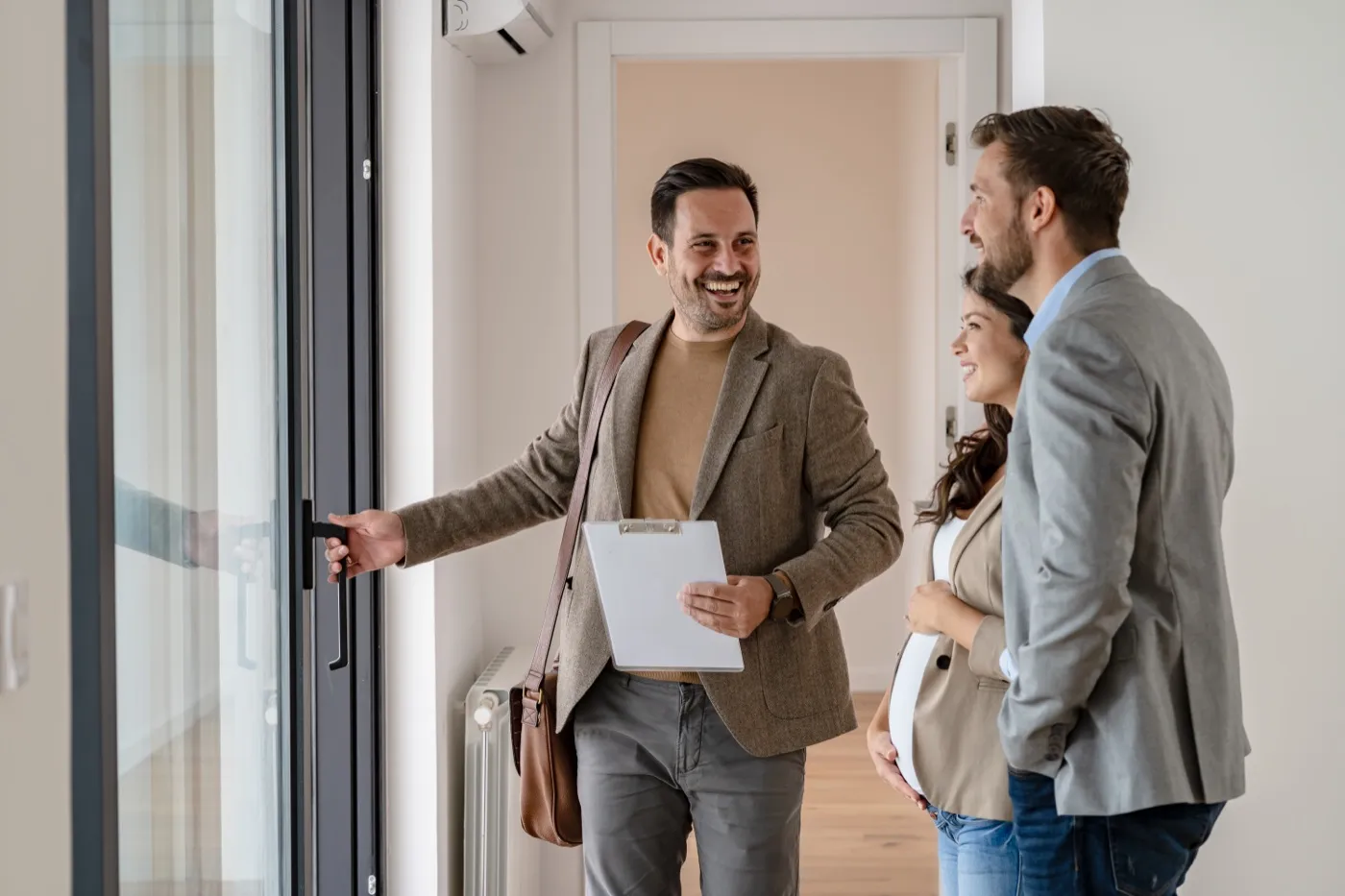 A real-estate agent with a clipboard showing a couple through a home